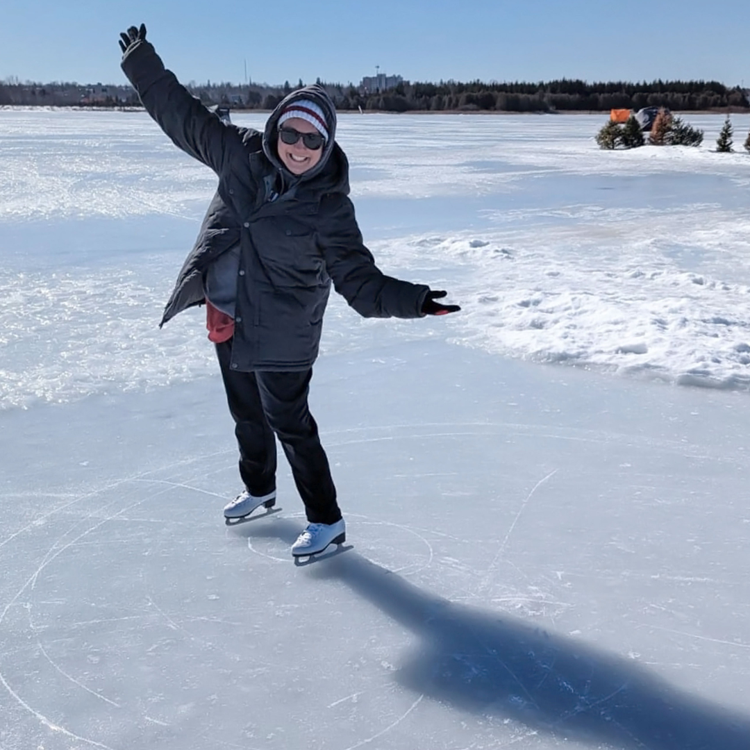 A smiling woman in winter apparel, skates on a groomed area of ice on a lake.